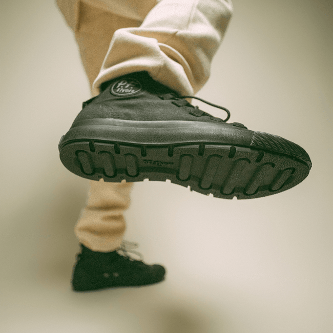 Black high-top sneaker worn by a person in beige sweatpants on a neutral background.