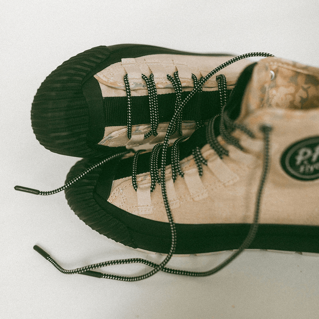 Pair of beige high-top sneakers with camo-print lining and black soles on a white background.