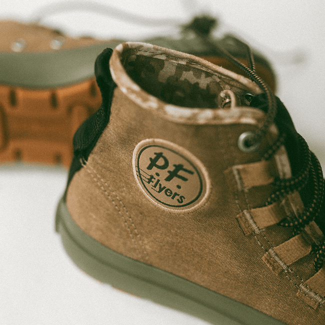 Close-up of a brown high-top sneaker with camo-printed lining on a white background.