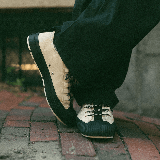 Close-up of a person wearing black-and-beige sneakers standing on brick pavement.