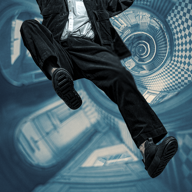 Person wearing black slip-on shoes and dark clothing in a surreal, abstract setting with blue and white patterns.