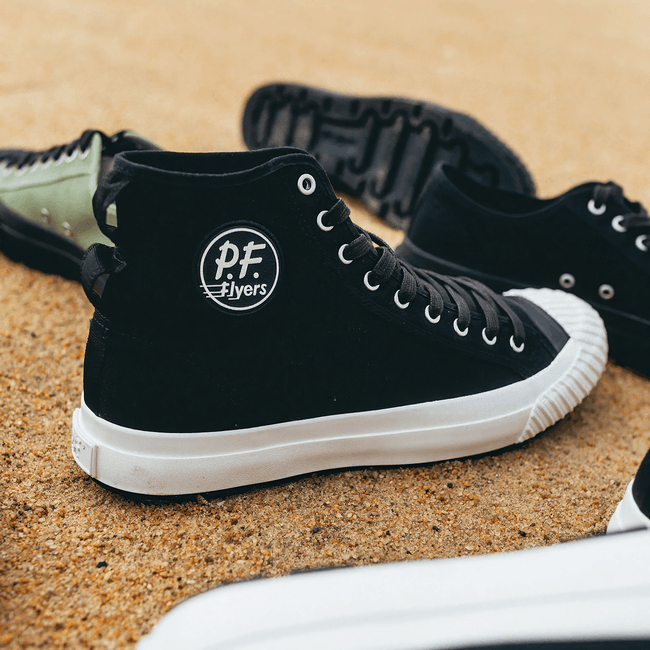 Close-up of a single black high-top sneaker with a white sole on a sandy surface.