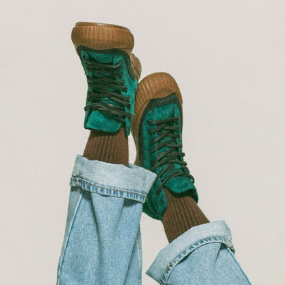 Green high-top sneakers with gum soles worn with light blue jeans on a plain background