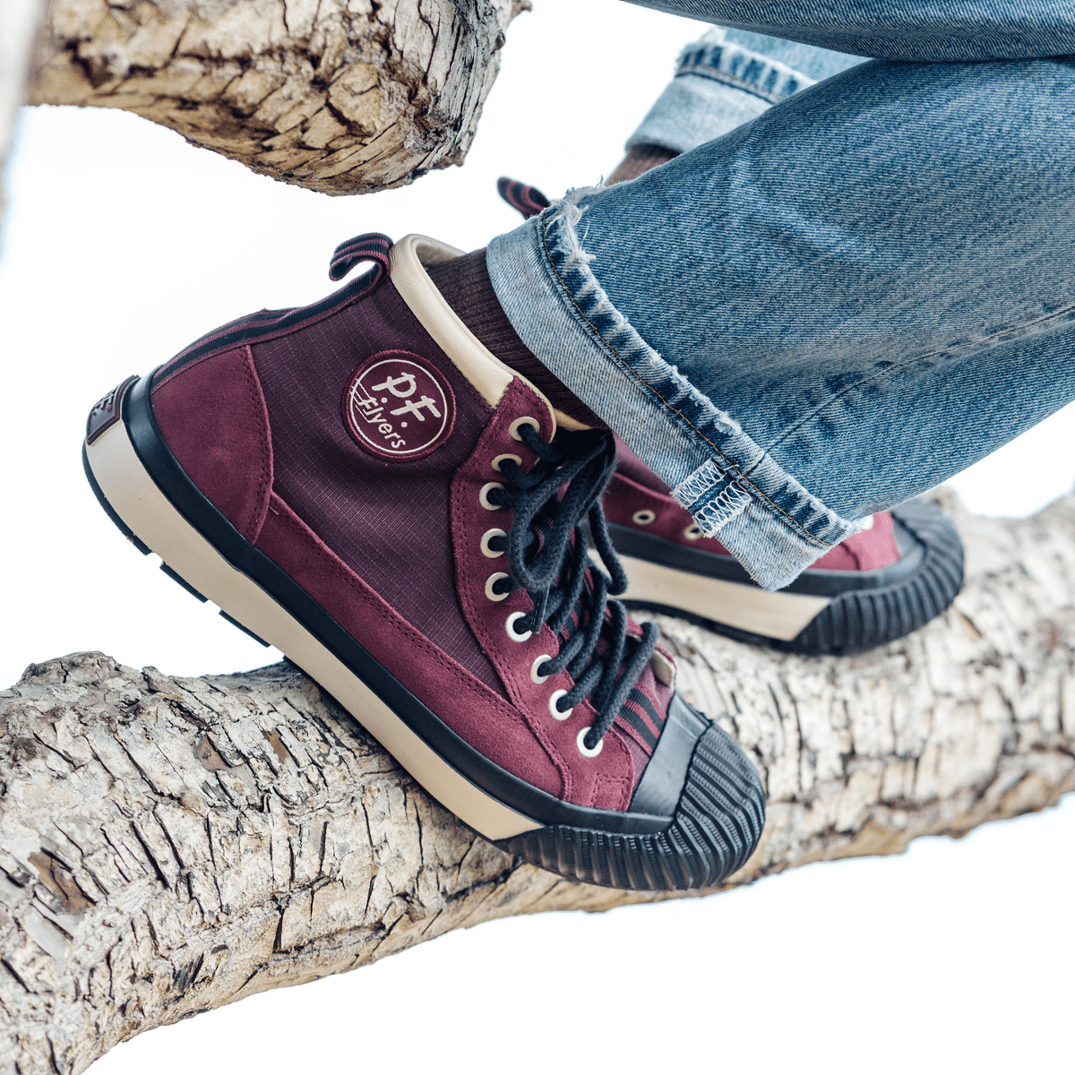 Burgundy high-top sneakers with black-and-white accents on a tree branch.