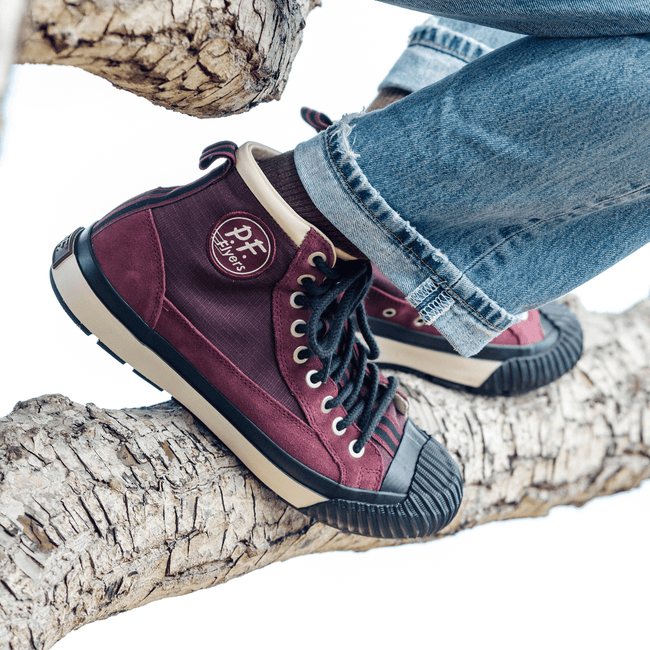 Burgundy high-top sneakers with black-and-white accents on a tree branch.