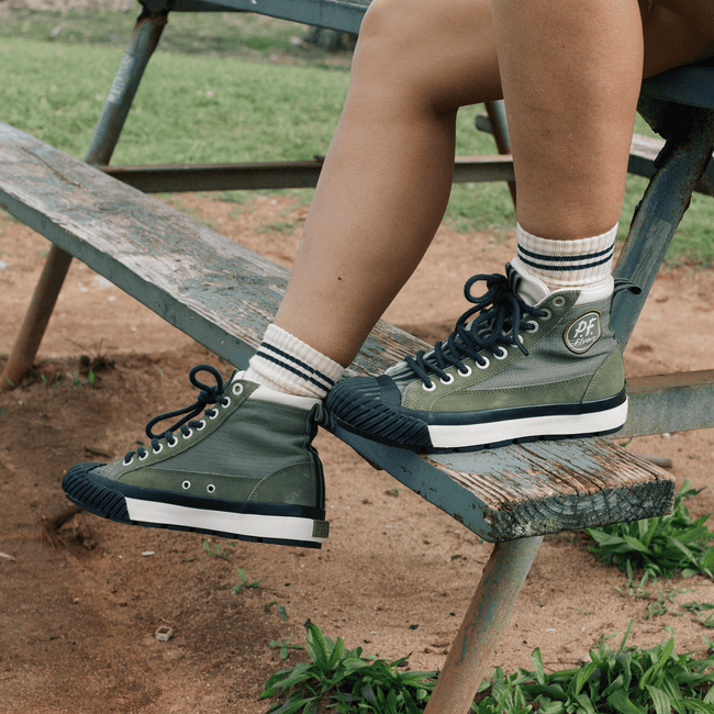 Person wearing green high-top sneakers with black-and-white accents on a wooden bench outdoors.