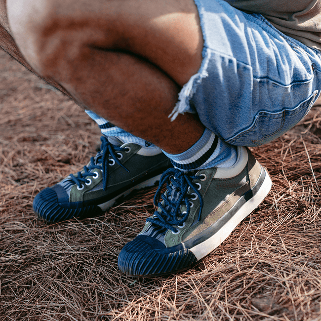 Person squatting on dry grass wearing green low-top sneakers with black detailing.