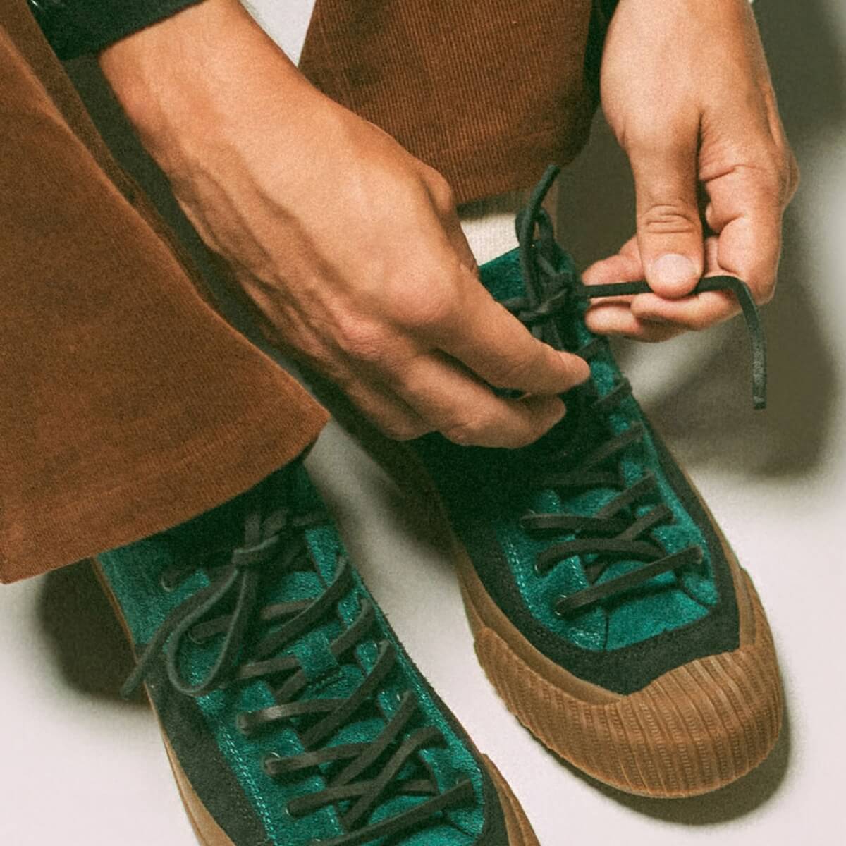 Person tying the laces of green and gum sneakers on a neutral background