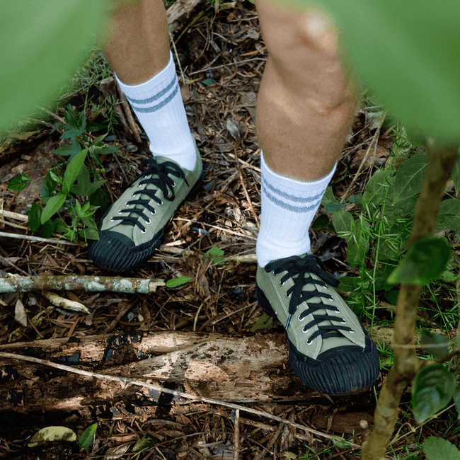 Person wearing green low-top sneakers with black soles standing on a forest floor.