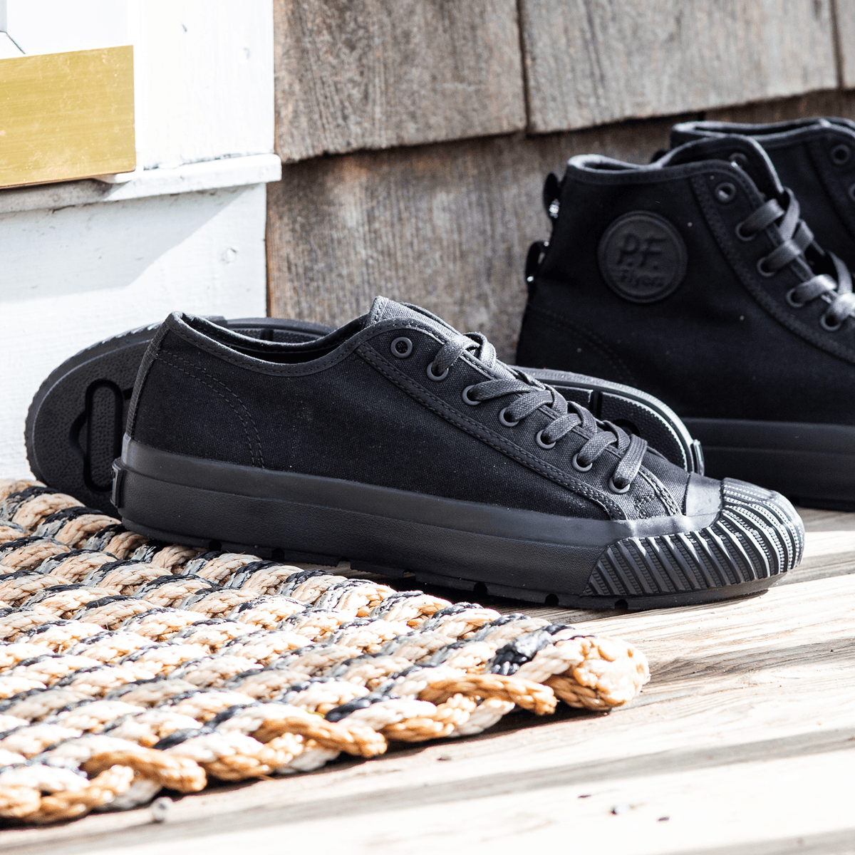Black low-top sneakers on a wooden porch with a woven mat.