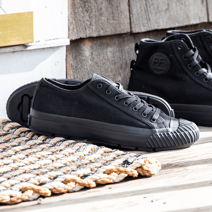 Black low-top sneakers on a wooden porch with a woven mat.