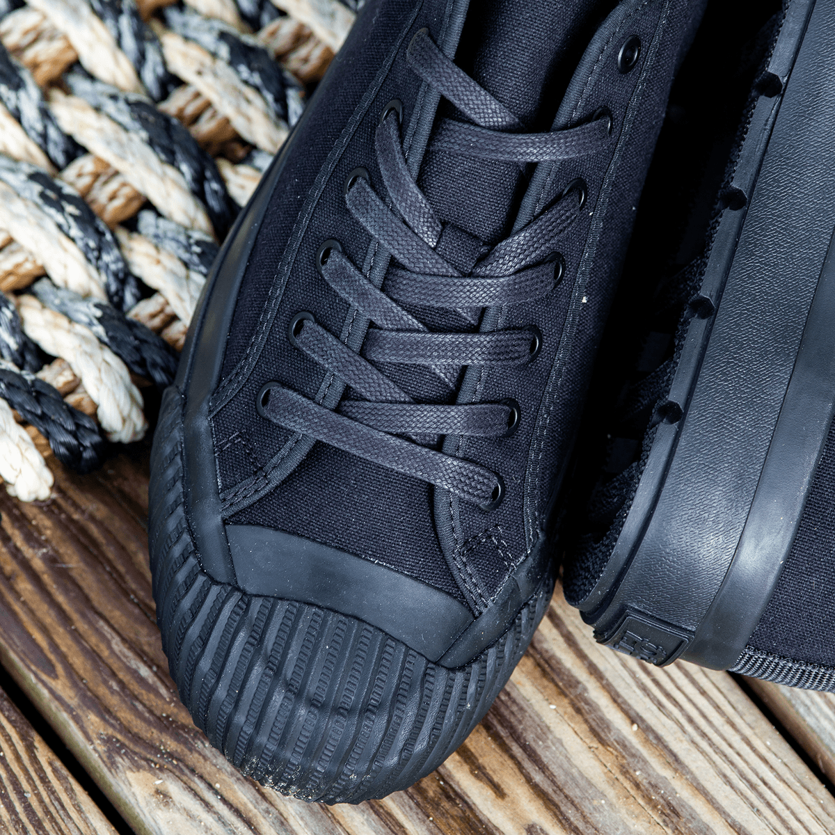 Close-up of black low-top sneakers on a wooden porch.
