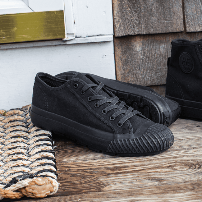 Black low-top sneakers on a wooden porch with a woven mat.
