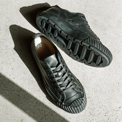 Pair of black leather low-top sneakers on a concrete floor.