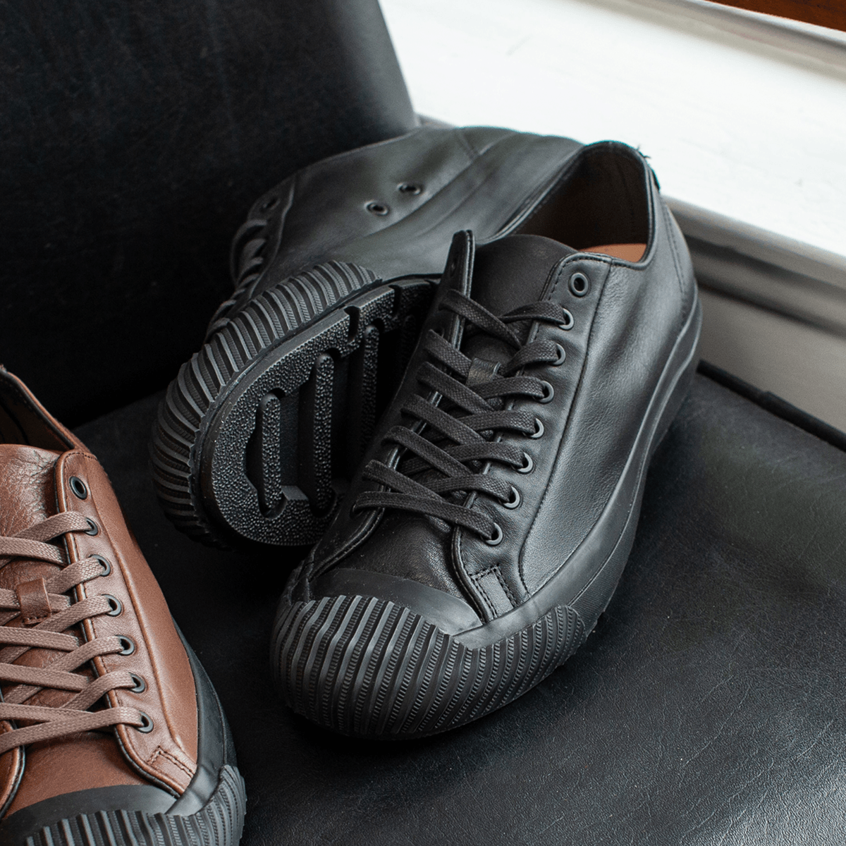 Black leather low-top sneakers on a chair.