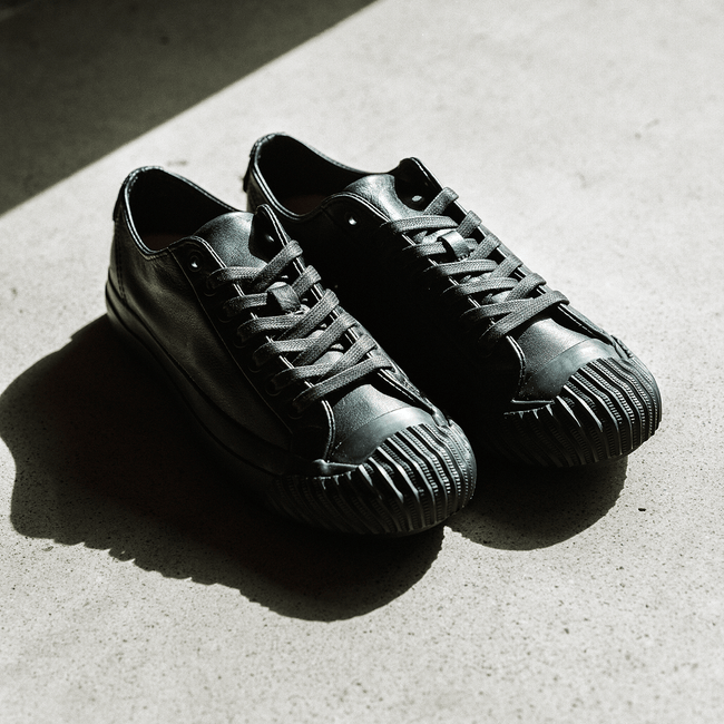 Pair of black leather low-top sneakers on a concrete floor.