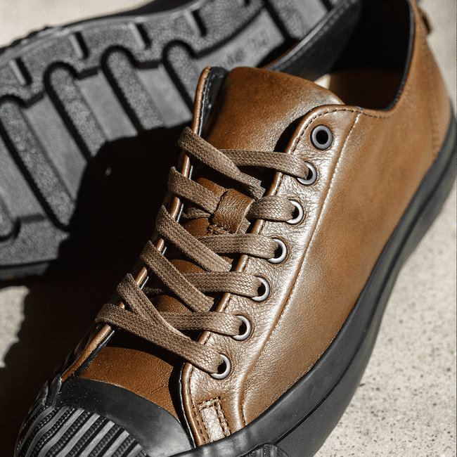 Close up of brown leather low-top sneakers with black soles on a concrete floor.