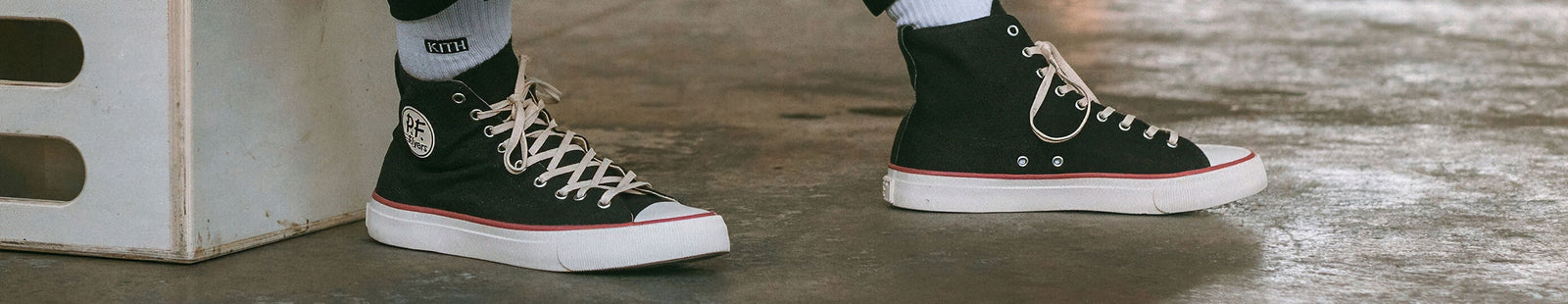 Black high-top sneakers with white soles on a concrete floor.