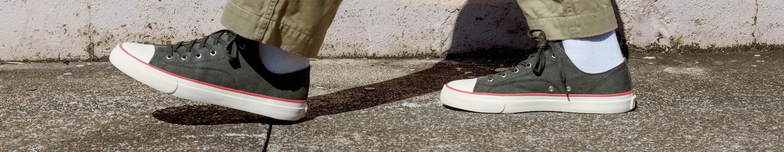 Person wearing black low-top sneakers with red accents on a concrete surface.