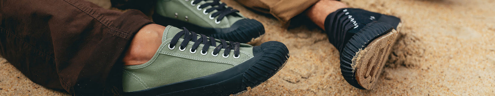Close-up of green and black low-top sneakers on a sandy surface.