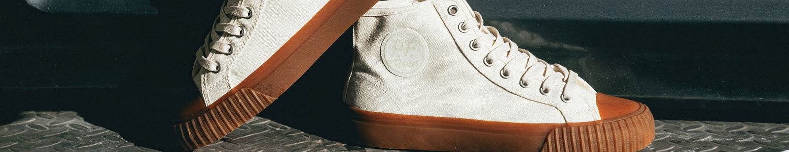 White high-top sneakers with brown soles on a truck bumper.