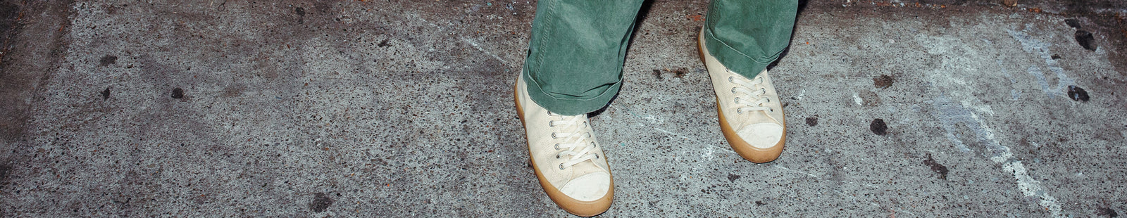 Close-up shot of a person wearing off-white low-top sneakers with tan soles on a concrete floor.