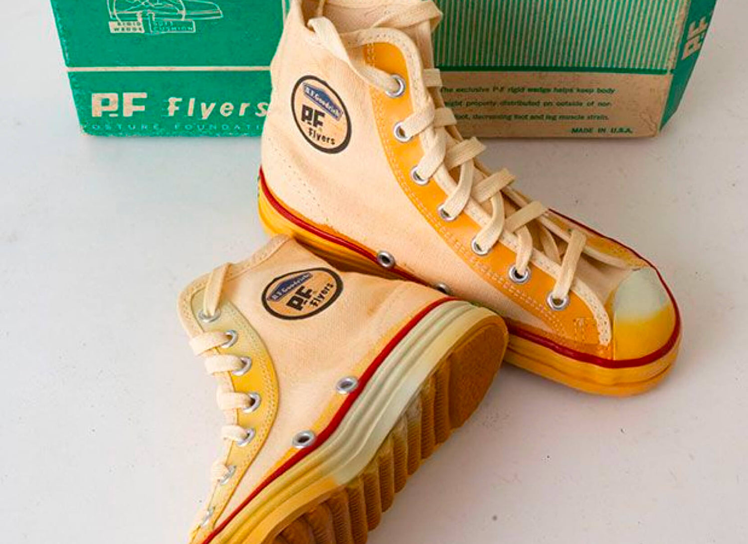 Pair of retro P.F. Flyers high-top sneakers with a green shoebox in the background.