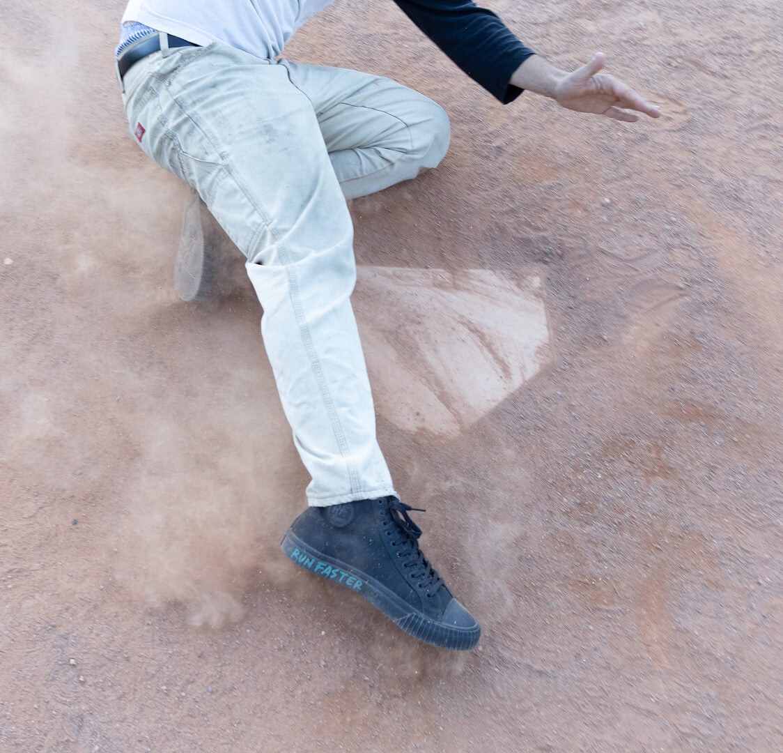 Person sliding on a field wearing black high-top shoes.