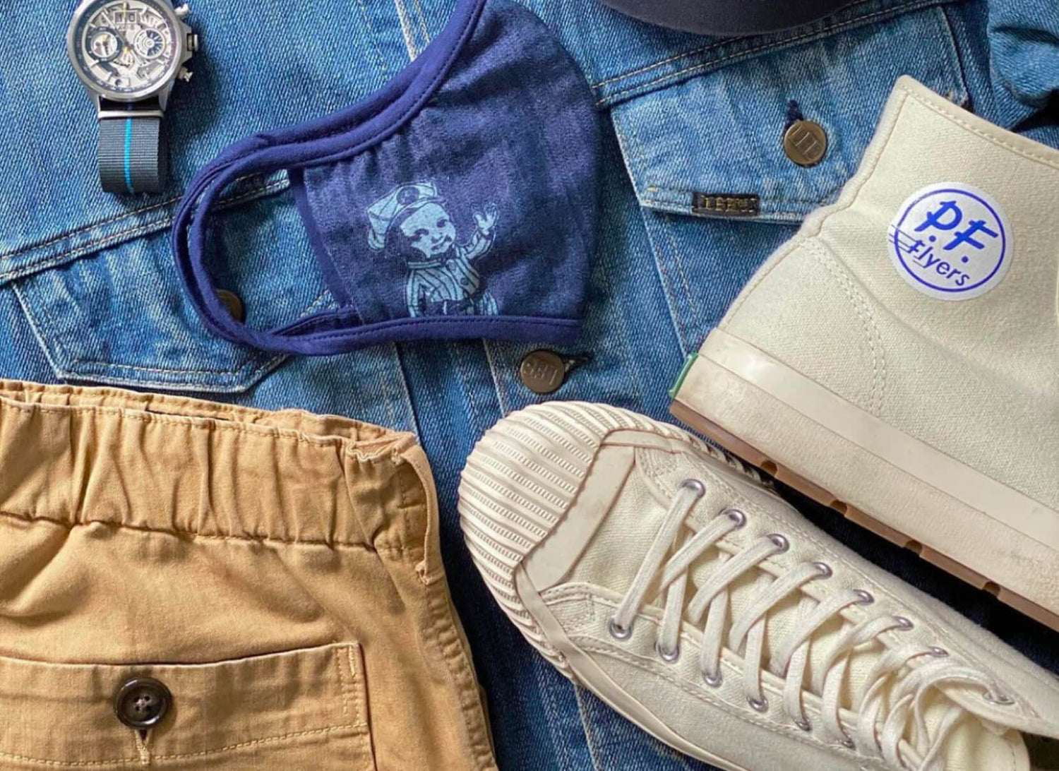 Collection of casual clothing and accessories including beige high-top sneakers, a blue denim jacket, tan pants, and a blue face mask.