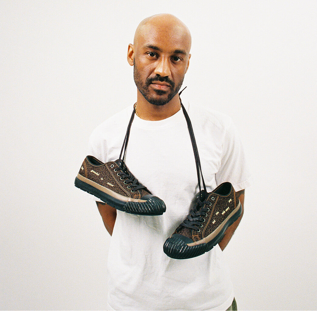 Brown low-top sneakers hanging by their laces around a man’s neck against a white background.