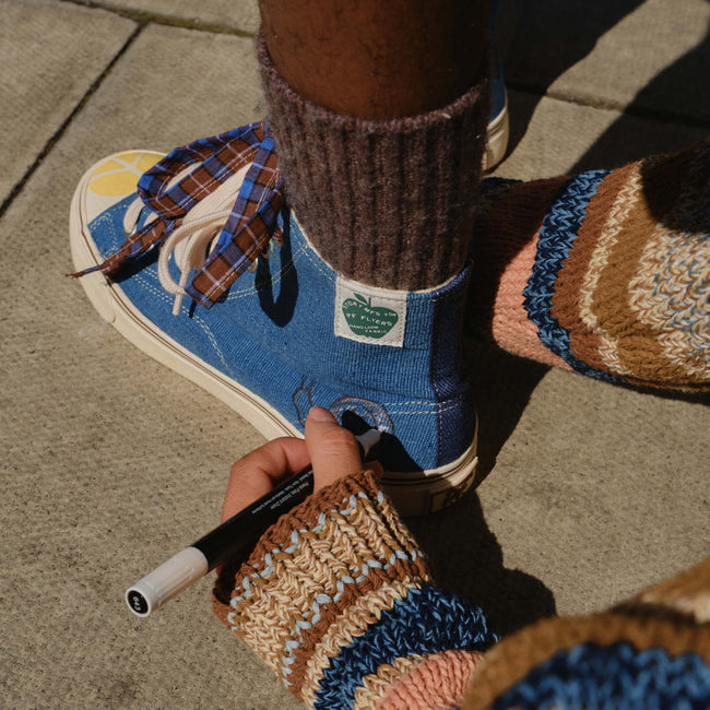 Close-up of a hand drawing on an indigo high-top sneaker with a marker.