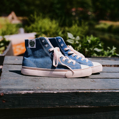 Pair of indigo high-top sneakers on a weathered wooden table with a blurred garden background.
