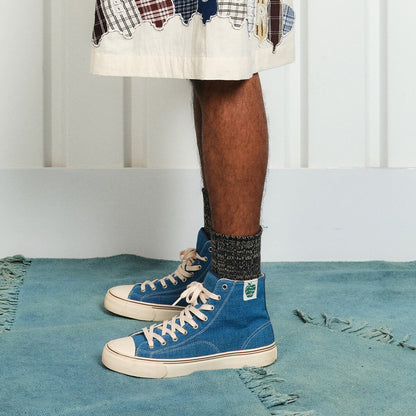 A person standing on a rug wearing indigo high-top sneakers.